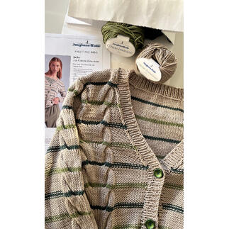 Wolljacke mit grünen Streifen und Knöpfen auf einem Tisch mit Garn und einer Anleitung.