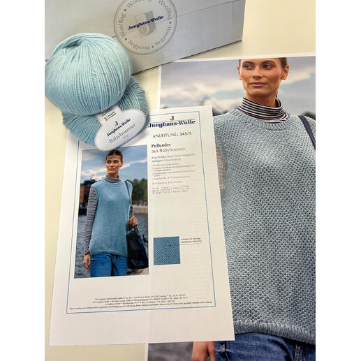 Wolle und Anleitung des hellblauen Pullunders auf einem Tisch mit Foto und Garn.