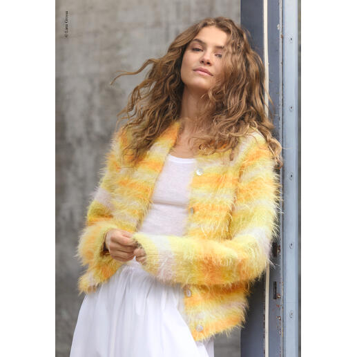 Frau in gelb-orange gestreifter Jacke aus Basta Mista steht an einer Wand.