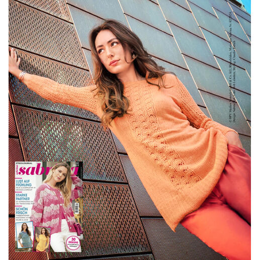 Frau in tailliertem Longpulli aus Charme steht vor einem modernen Gebäude.