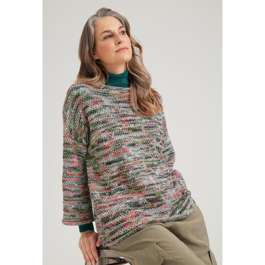 Frau sitzt in einem bunten Merino-Pullover auf einem Hocker.