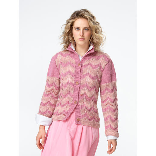 Frau steht in einer rosa Jacke mit Zopfmuster aus Landwolle.
