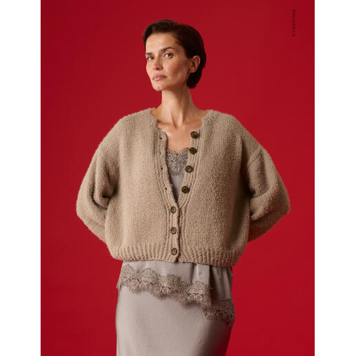 Beige Jacke aus Cosi mit Knöpfen, Modell steht vor rotem Hintergrund.