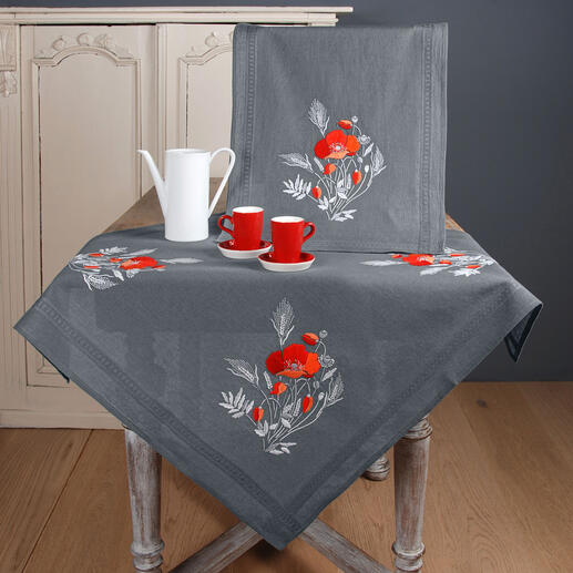 Tischdecke und Servietten mit Mohnblumenmotiven auf gedecktem Tisch.