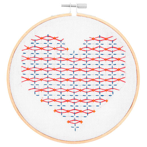 Stickbild in Herzform mit rot-blauen Mustern auf weißem Hintergrund.