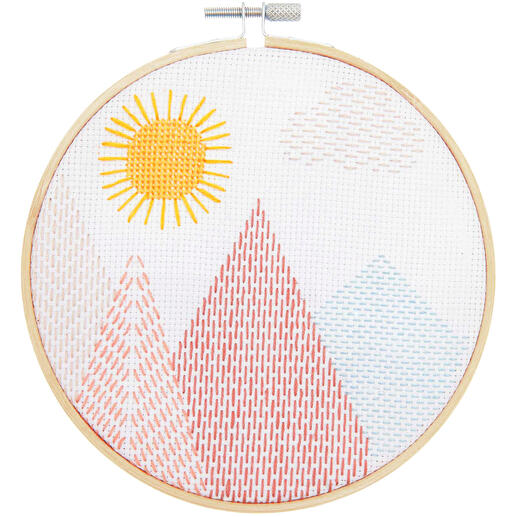 Stickbild mit einer Landschaft, Bergen und Sonne, in warmen Farben auf weißem Hintergrund.