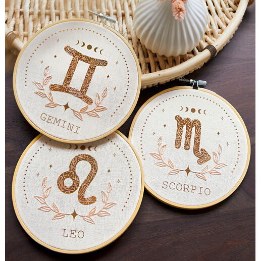 Drei Muster von minimalistischer Tierkreis-Stickerei auf einem Tisch.