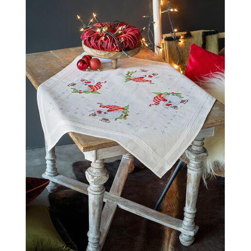 Tischdecke mit Wichteln und winterlicher Dekoration auf einem Holztisch.