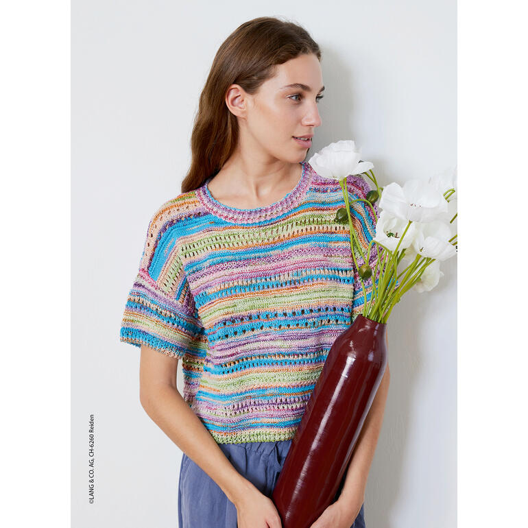 Frau trägt einen bunten, gestreiften Kurzarmpullover und hält eine Vase mit weißen Blumen.