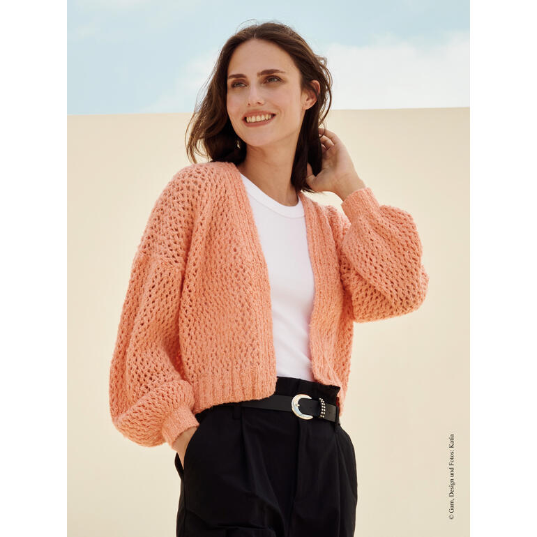 Frau in korallfarbener Jacke aus Pluma mit weichem Gesichtsausdruck.