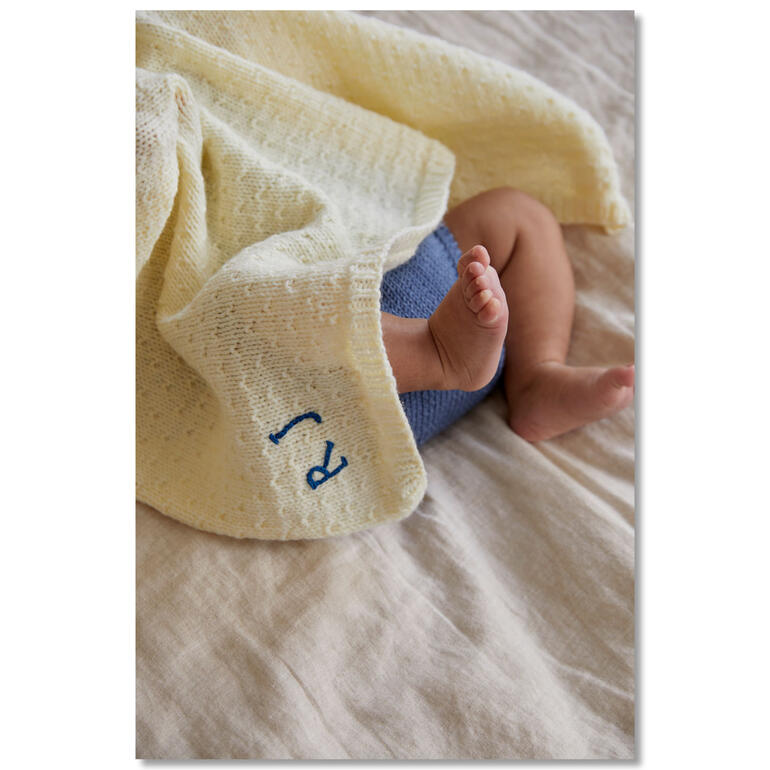 Babydecke umhüllt ein Baby mit einem blauen Strampler.