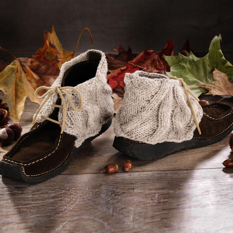 Anleitung 808/1: Schuhstulpen aus Landwolle, braun, auf einem Holzfußboden.