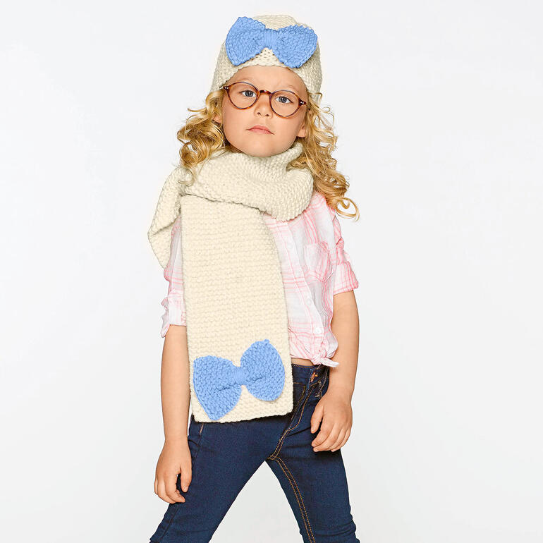 Mütze und Schal aus Merino Dick, mit großen blauen Schleifen, getragen von einem Kind.