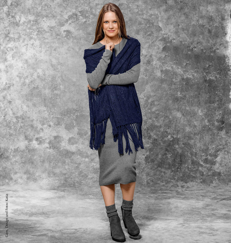 Frau trägt ein dunkelblaues Schultertuch mit Fransen über einem grauen Kleid, posiert vor grauem Hintergrund.