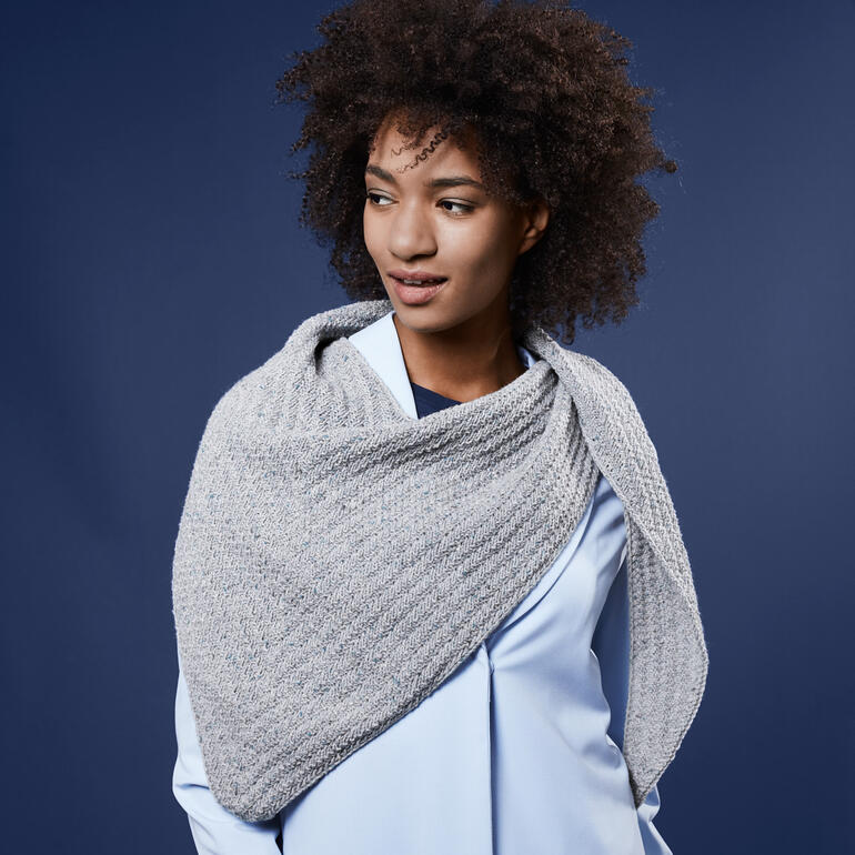 Dame trägt graues Tuch, lächelnd vor tiefblauem Hintergrund.