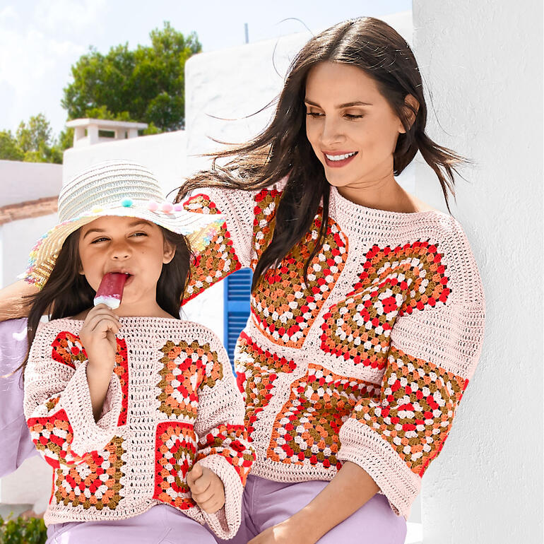 Frau und Mädchen tragen bunte Häkelpullis aus Cotonia II und genießen einen sonnigen Tag.