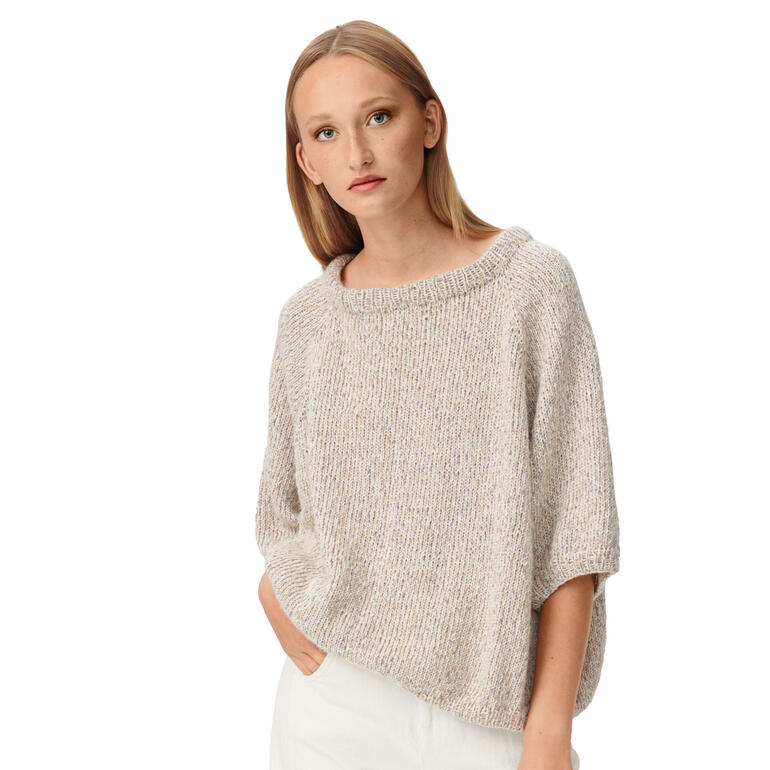 Frau sitzt in einem gemütlichen, beigen Pullover vor neutralem Hintergrund.