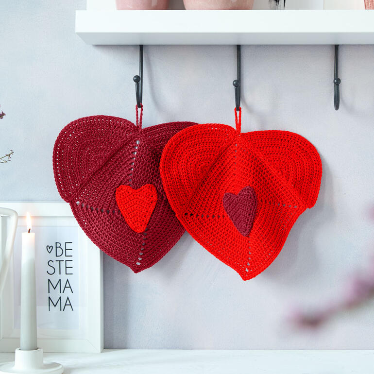 Zwei rote und burgunderfarbene Herz-Topflappen an einer Wand aufgehängt.