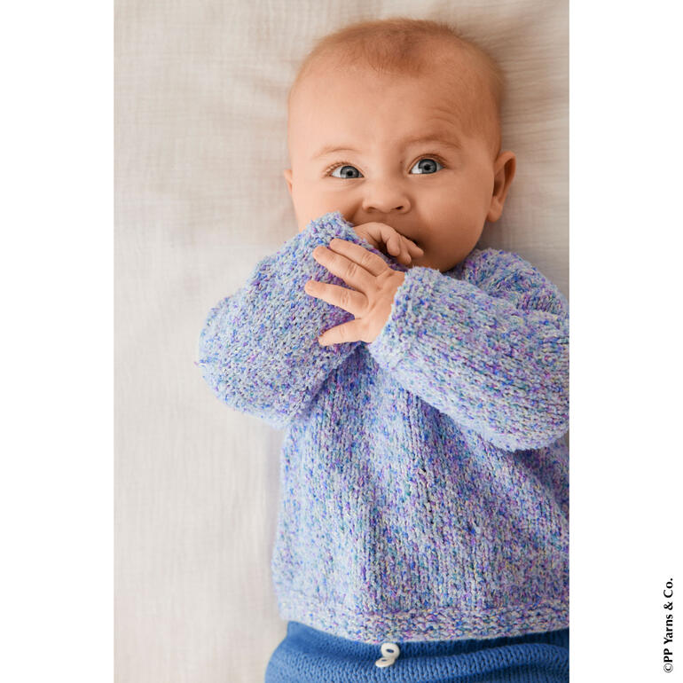 Baby in lila Pullover aus Phil Tutti Frutti liegt auf einem Bett.