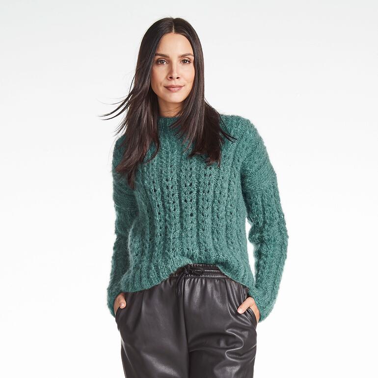Frau in grünem Pullover mit Struktur und langen Ärmeln vor hellen Hintergrund