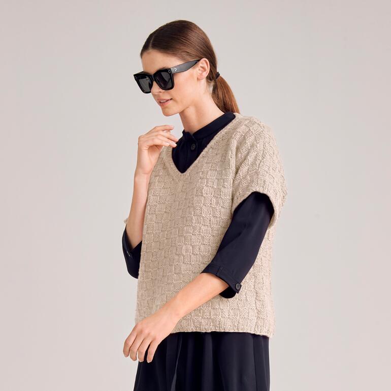 Frau in beigem Pullover aus grober Strick vor neutralem Hintergrund