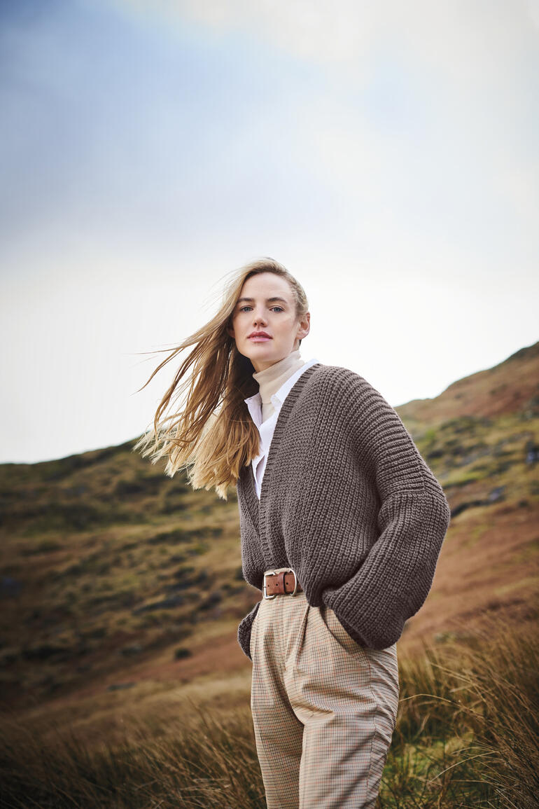 Frau in braunem, grob gestricktem Cardigan über einem weißen Hemd