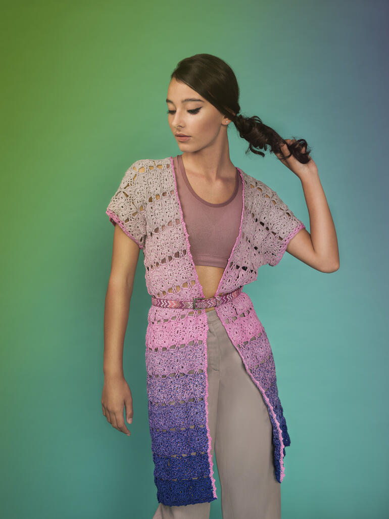 Frau in buntem Häkelmantel aus Zauberperlen® Cotton, posiert vor einem Farbverlauf.