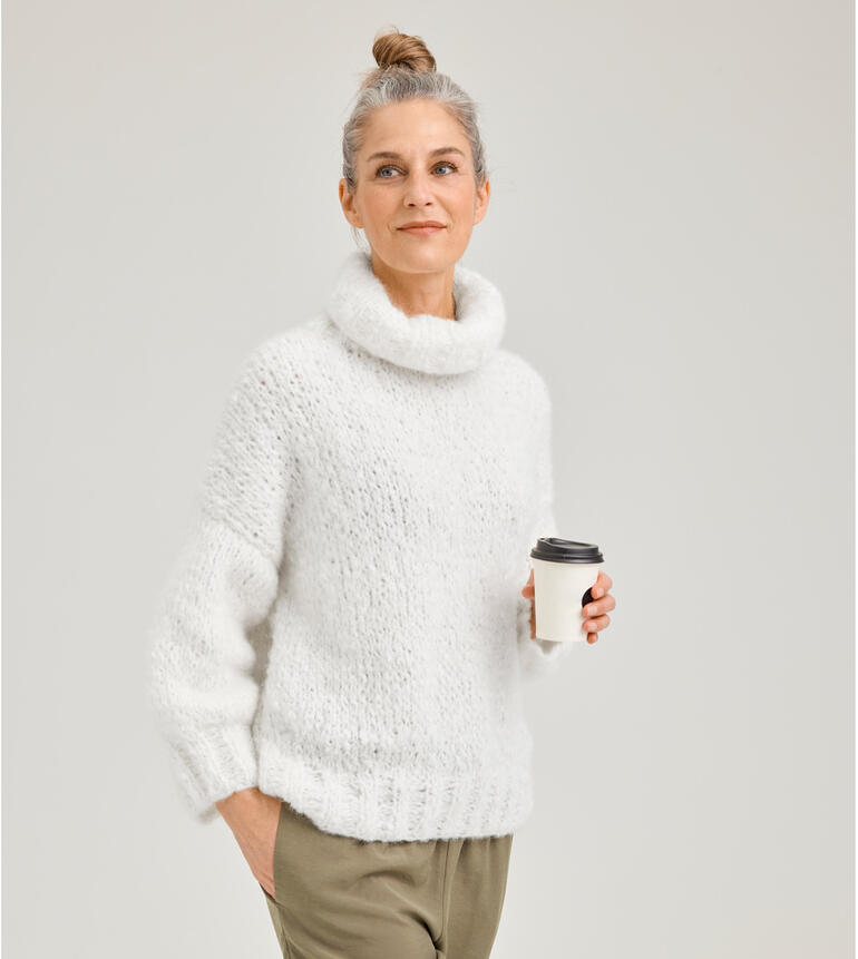 Frau in flauschigem weißen Pullover hält einen Kaffeebecher in der Hand.