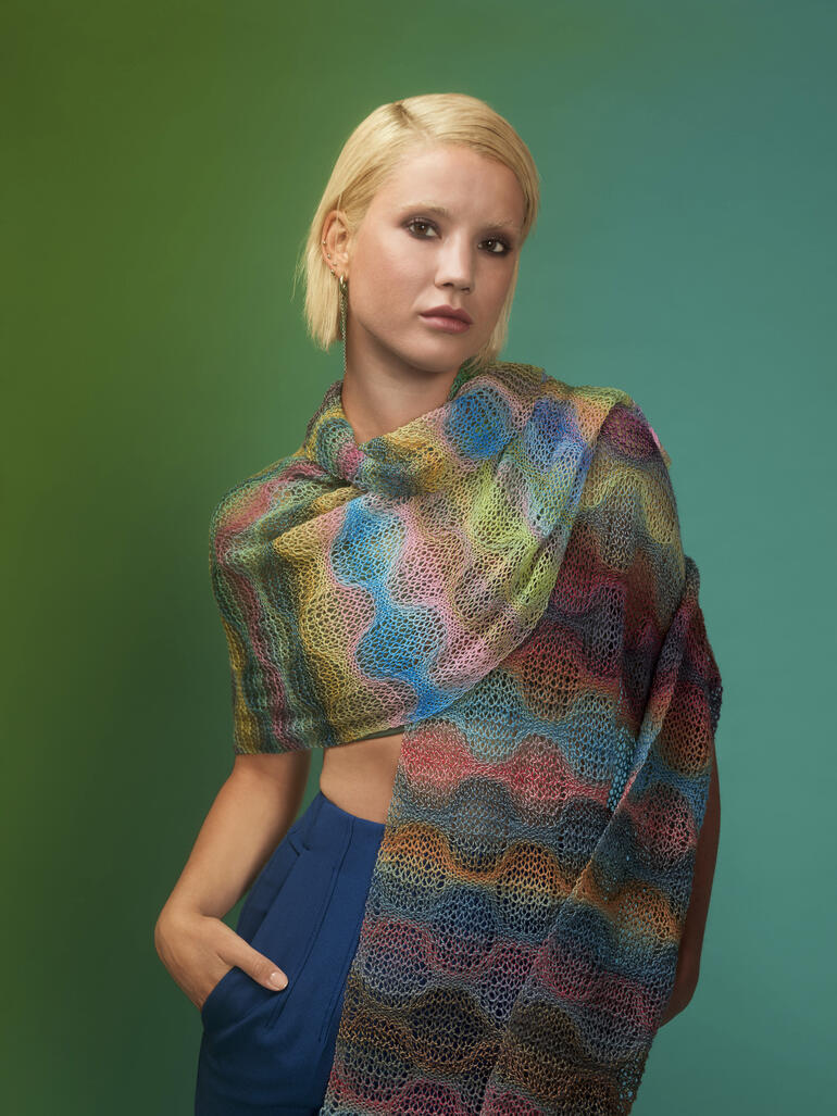 Frau zeigt eine bunte Stola aus Edition 6 von Schoppel Wolle und posiert stilvoll.