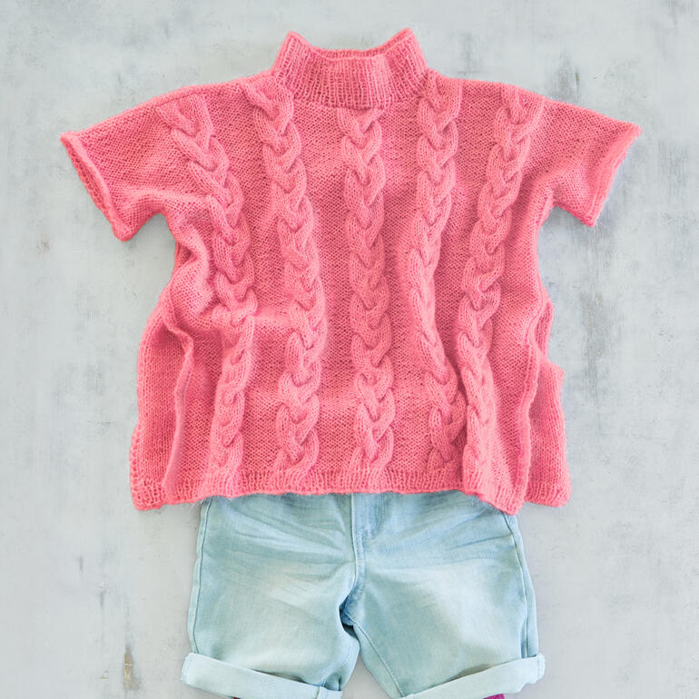 Rosa Poncho aus Cielo Wolle mit Zopfmuster in einer neutralen Umgebung.