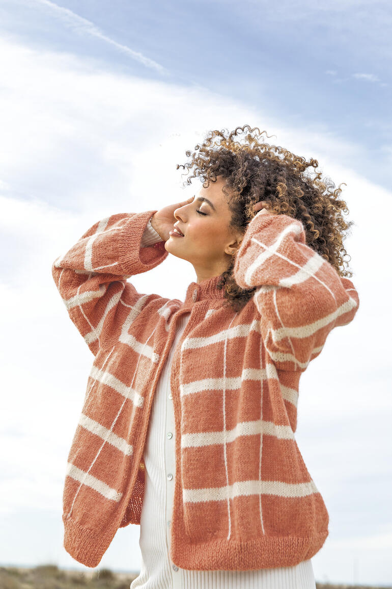 Rosa Jacke aus Soft Gratté Wolle mit weißen Streifen, getragen von einer Frau in der Natur.