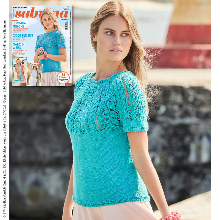 Netzpulli mit Ajour-Zopfpasse in Türkis, lächelnd am Strand.