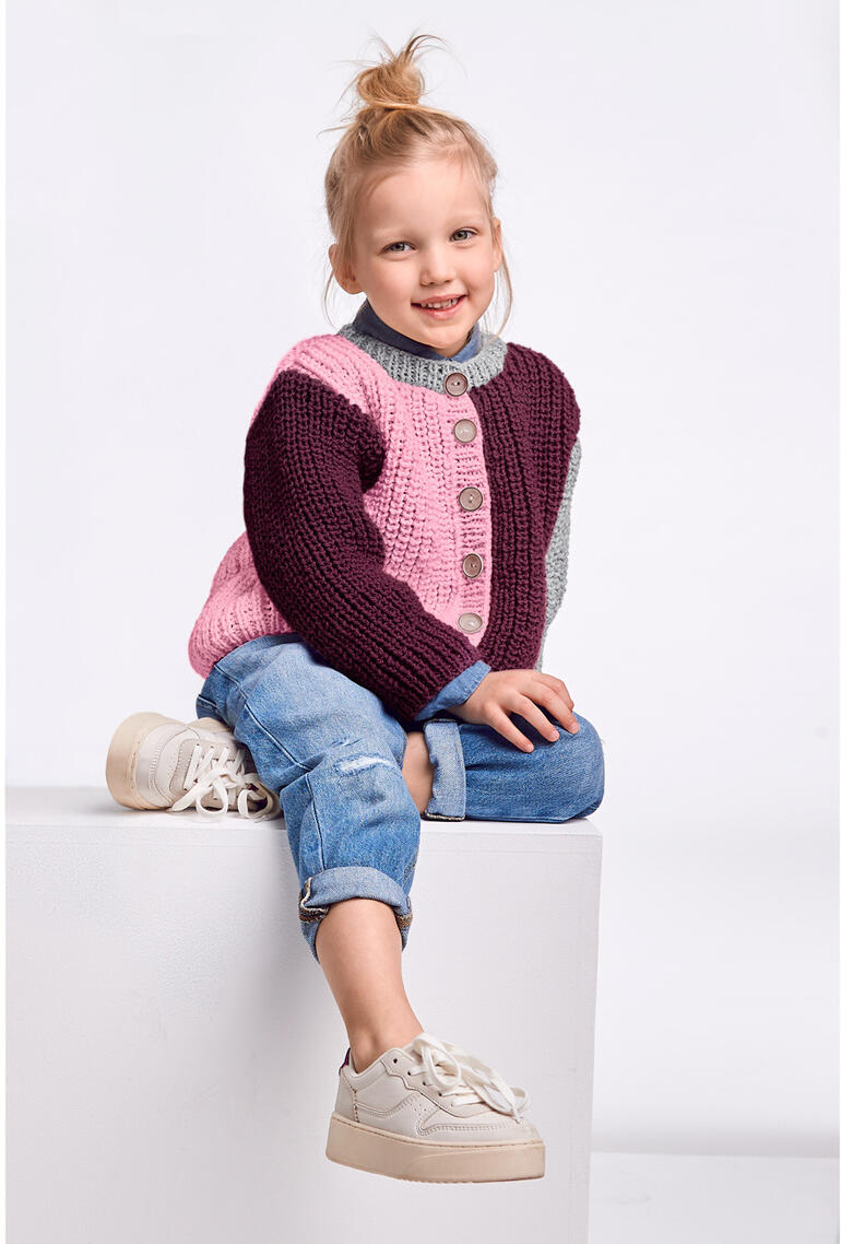 Mädchen sitzt in modischer Kinderjacke aus Landwolle, trägt Jeans und Sneakers.