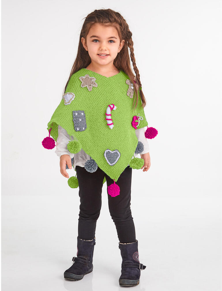 Mädchen trägt einen grünen Poncho mit bunten Applikationen, steht fröhlich.