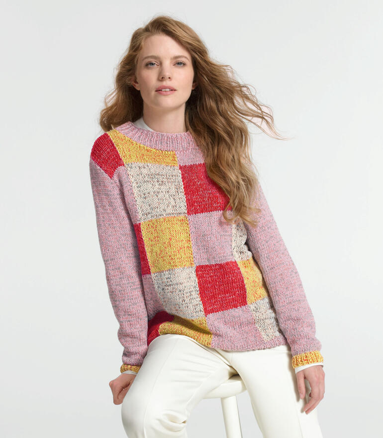 Frau in pink-rot-gemustertem Pullover sitzt lässig und schaut in die Kamera.