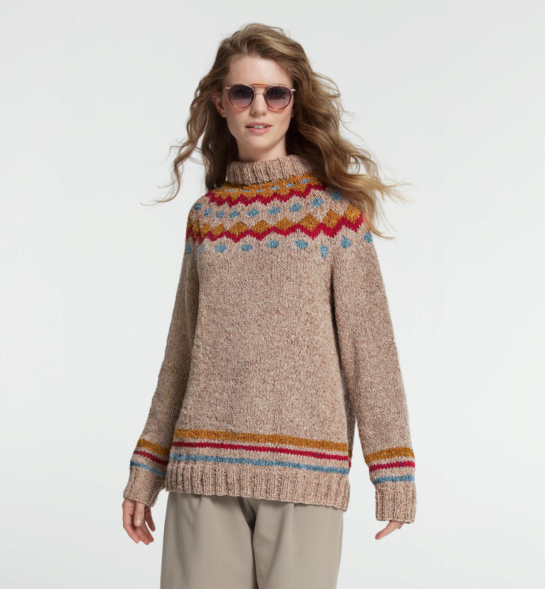 Frau in beigem Pullover mit farbigen Stripes und Sonnenbrille lächelt in die Kamera.