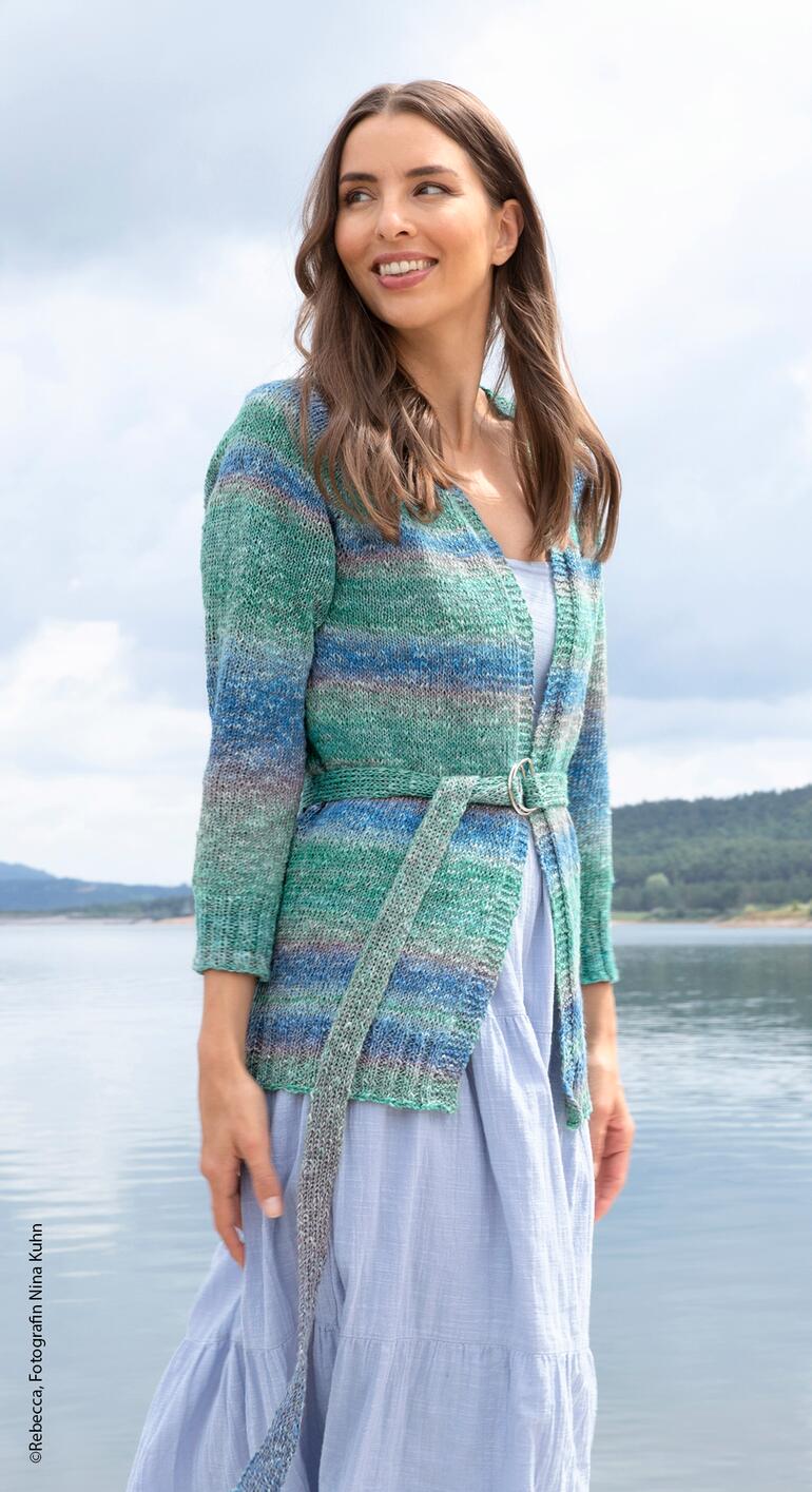 Frau in gestreifter Jacke steht am Wasser und lächelt ins Freie.