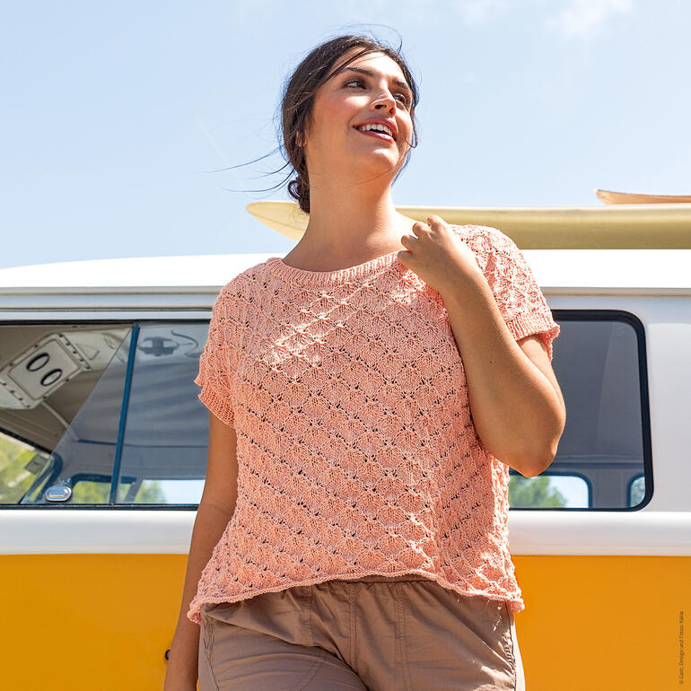 Frau im luftigen Pulli aus Aqua vor einem gelben VW-Bus.
