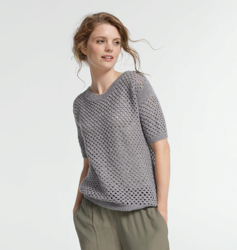 Frau in grauem, luftigem Pullover auf hellem Hintergrund.