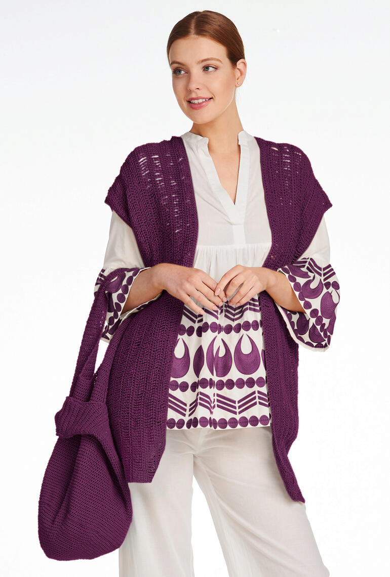 Häkelweste in lila, kombiniert mit einer weißen Bluse mit Druck.