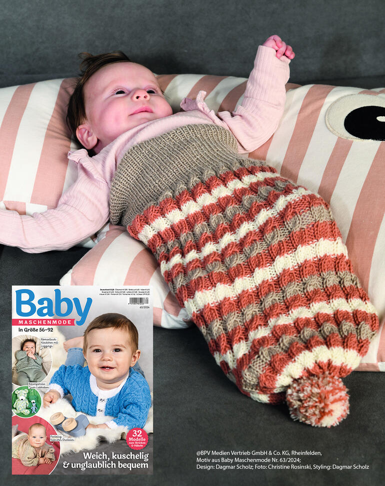 Baby liegt in einem Pucksack und Decke aus Nuovo Merino 180, entspannt auf einem Kissen.