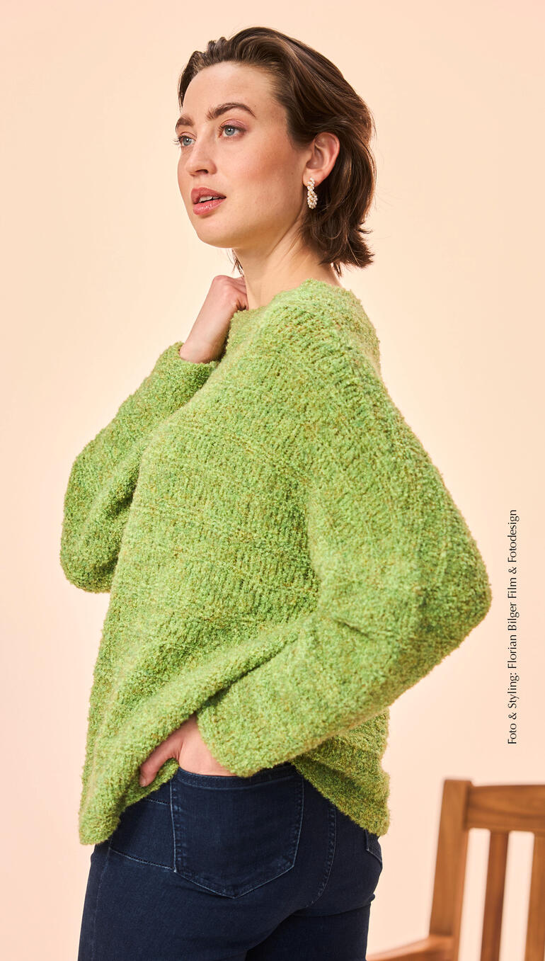Pullover aus Boucle in leuchtendem Grün, getragen von einer nachdenklichen Frau.