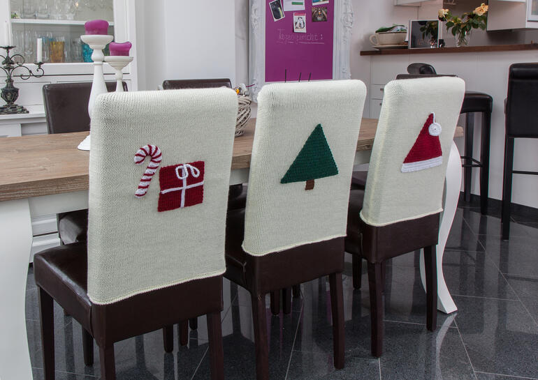 Gestickte Stuhlhussen mit weihnachtlichen Motiven auf einem Tisch.