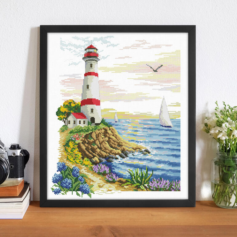 Stickbild eines Leuchtturms mit blühenden Blumen und Meer.