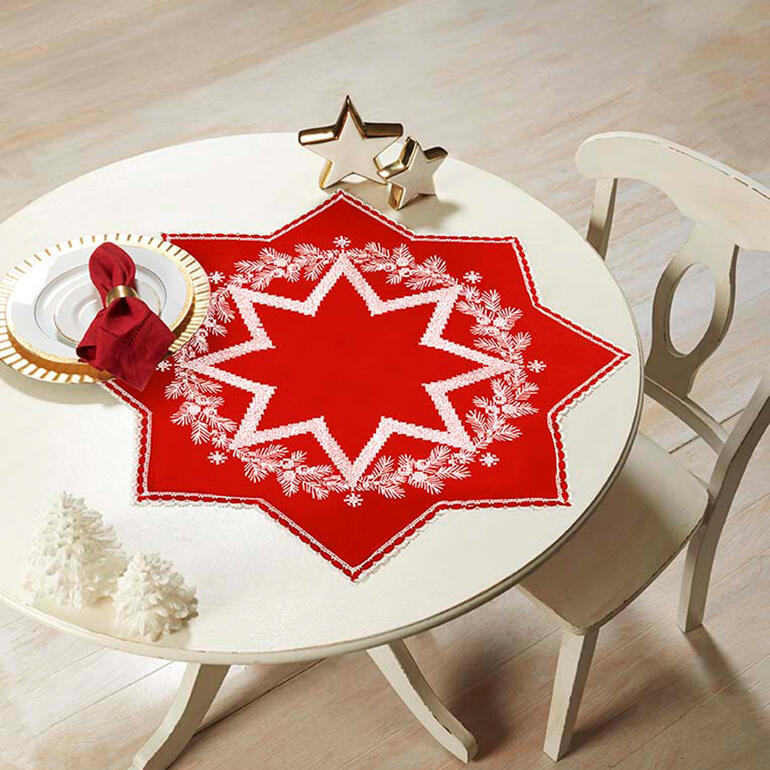 Rote Tischdecke mit weißer Stickerei in Sternform auf einem Tisch.