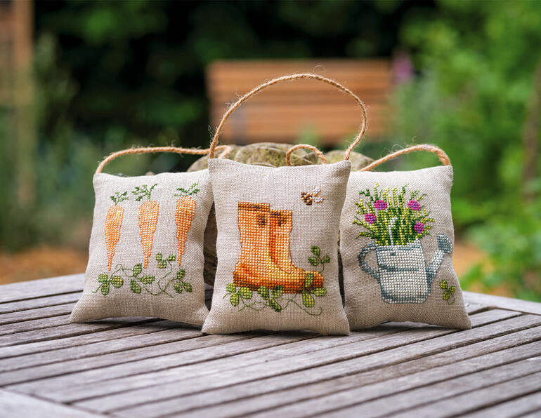 Drei Deko-Kissen im Garten-Design, mit Stiefeln und Gartenwerkzeugen verziert.