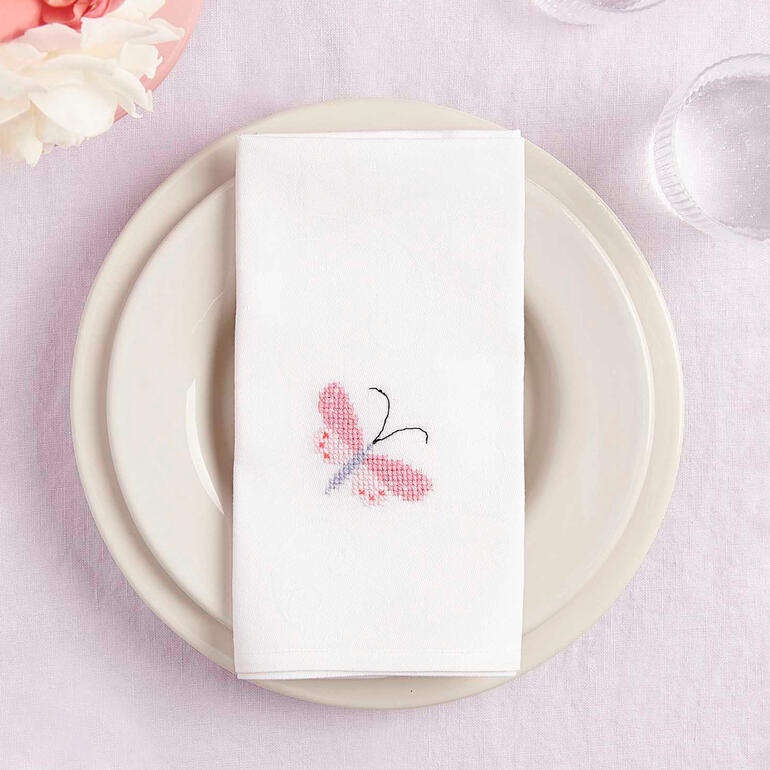 Serviette mit Schmetterlings-Stickerei, dekorativ auf einem Teller angerichtet.